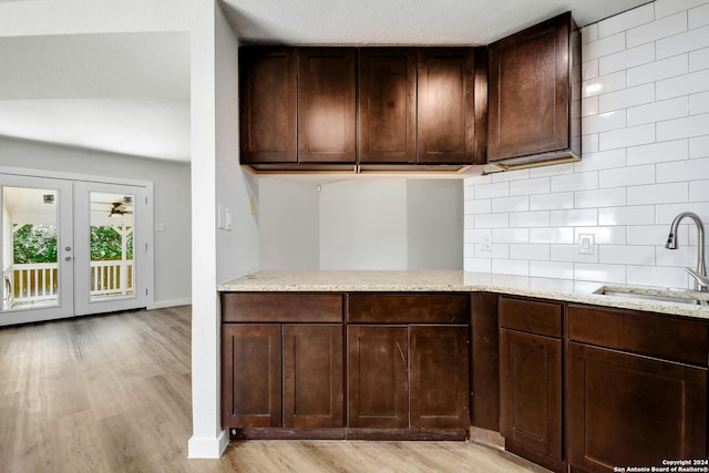 kitchen with dark brown cabinets, backsplash, light stone countertops, light wood-type flooring, and sink