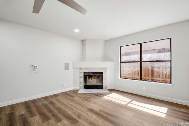 unfurnished living room featuring hardwood / wood-style floors, a tiled fireplace, and ceiling fan