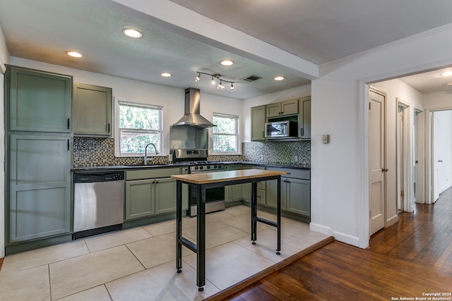 kitchen featuring wall chimney exhaust hood, green cabinets, stainless steel appliances, sink, and light hardwood / wood-style floors