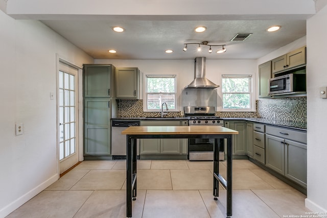 kitchen with decorative backsplash, wall chimney exhaust hood, sink, light tile patterned floors, and appliances with stainless steel finishes