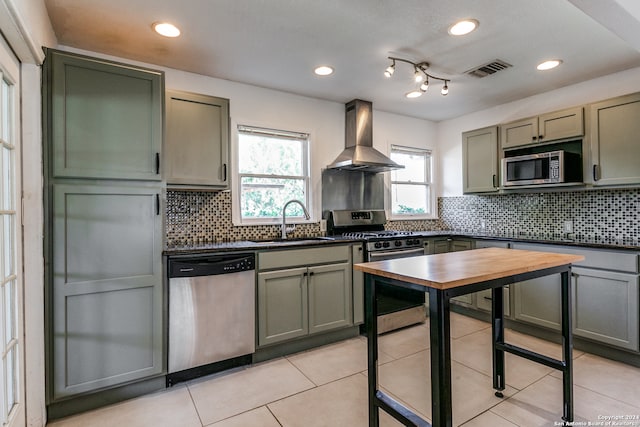 kitchen featuring wall chimney range hood, stainless steel appliances, sink, and backsplash