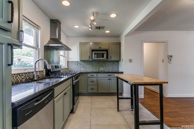 kitchen with wall chimney range hood, sink, appliances with stainless steel finishes, green cabinets, and decorative backsplash