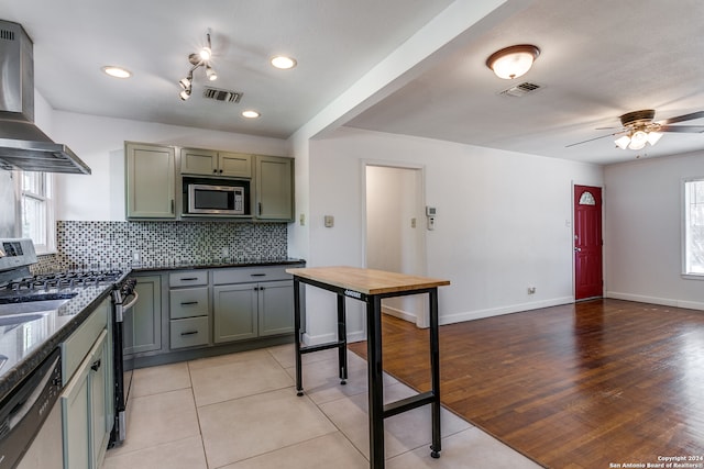 kitchen with appliances with stainless steel finishes, wall chimney range hood, light wood-type flooring, and a wealth of natural light