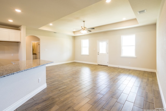 unfurnished living room featuring hardwood / wood-style floors, a tray ceiling, and ceiling fan