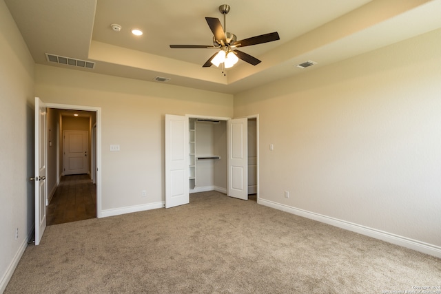 unfurnished bedroom with ceiling fan, a tray ceiling, and carpet floors