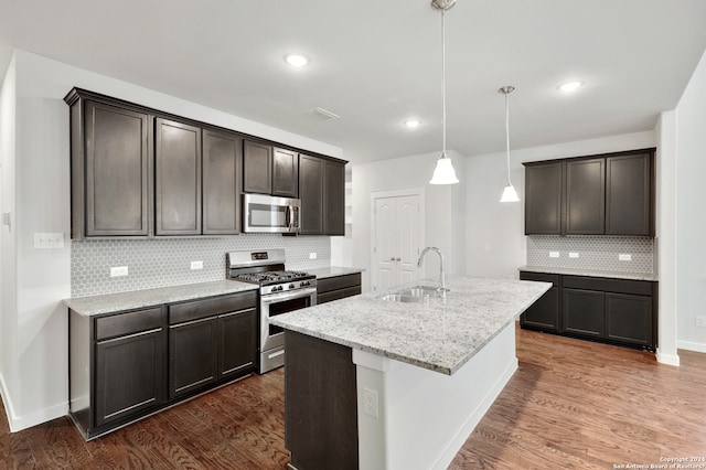 kitchen with sink, an island with sink, stainless steel appliances, decorative light fixtures, and dark wood-type flooring