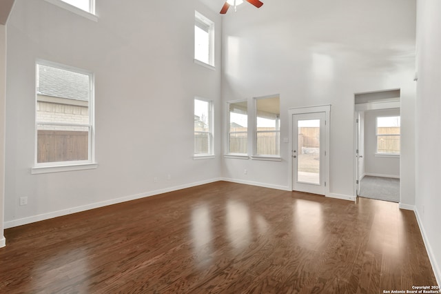 unfurnished living room featuring dark wood-type flooring, ceiling fan, a healthy amount of sunlight, and a towering ceiling