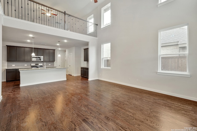 unfurnished living room with ceiling fan, a high ceiling, a wealth of natural light, and dark hardwood / wood-style floors