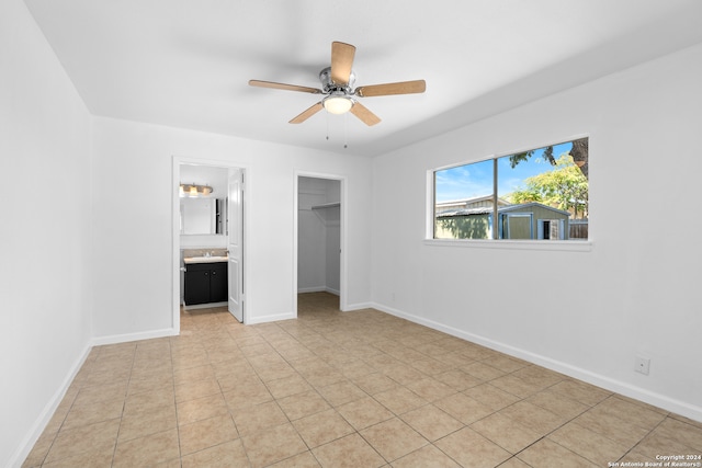 unfurnished bedroom with a walk in closet, ceiling fan, ensuite bathroom, light tile patterned flooring, and a closet