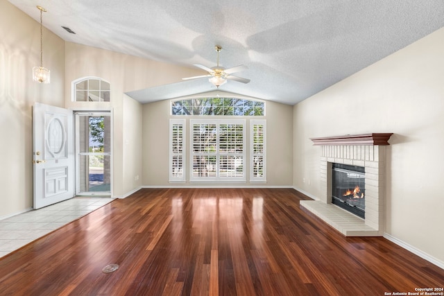 unfurnished living room featuring ceiling fan, a textured ceiling, wood-type flooring, vaulted ceiling, and a brick fireplace