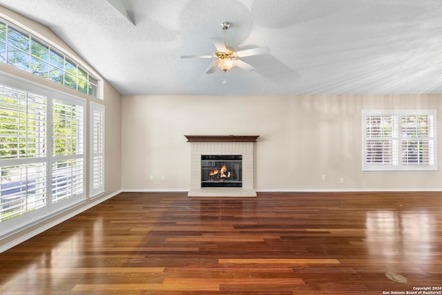 unfurnished living room with lofted ceiling, dark wood-type flooring, a brick fireplace, a textured ceiling, and ceiling fan