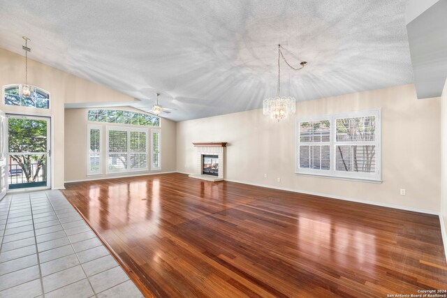 unfurnished living room featuring lofted ceiling, hardwood / wood-style floors, a textured ceiling, and ceiling fan with notable chandelier