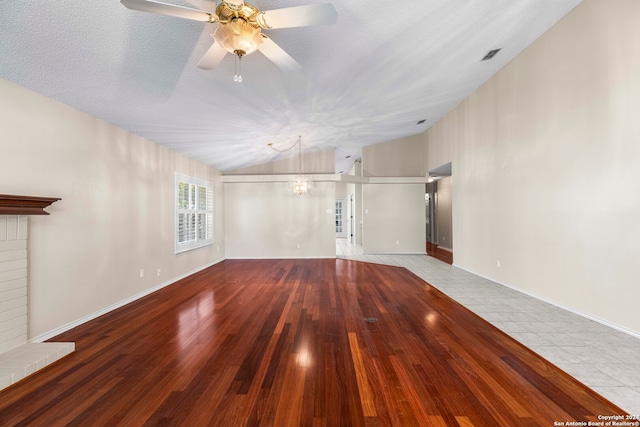 unfurnished living room featuring light wood-type flooring, a fireplace, a textured ceiling, ceiling fan, and vaulted ceiling