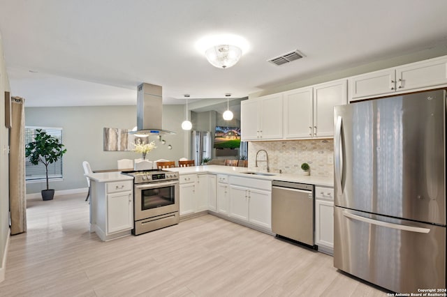 kitchen featuring kitchen peninsula, island exhaust hood, white cabinets, appliances with stainless steel finishes, and pendant lighting