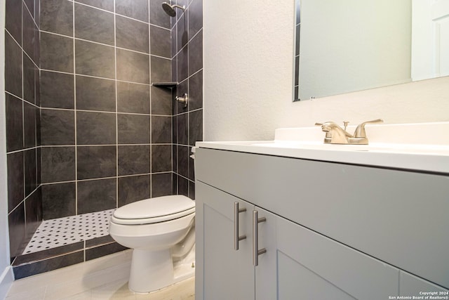 bathroom featuring vanity, toilet, tiled shower, and tile patterned flooring