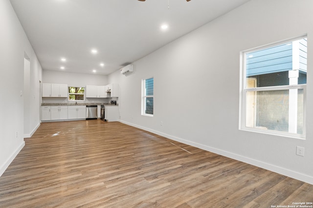 unfurnished living room featuring a wall unit AC, light hardwood / wood-style floors, and ceiling fan