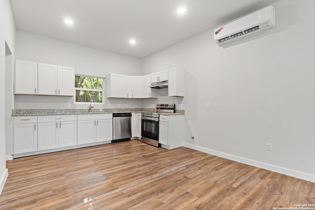 kitchen with light hardwood / wood-style floors, a wall unit AC, white cabinetry, and stainless steel appliances