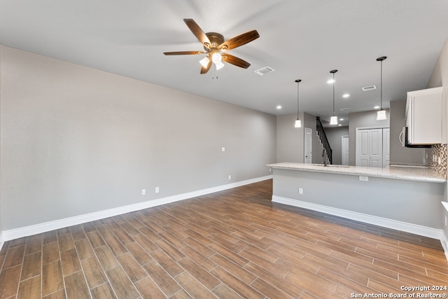 kitchen with light hardwood / wood-style flooring, hanging light fixtures, light stone countertops, white cabinetry, and ceiling fan