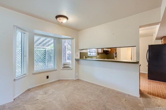 kitchen with light carpet, oven, kitchen peninsula, and black refrigerator