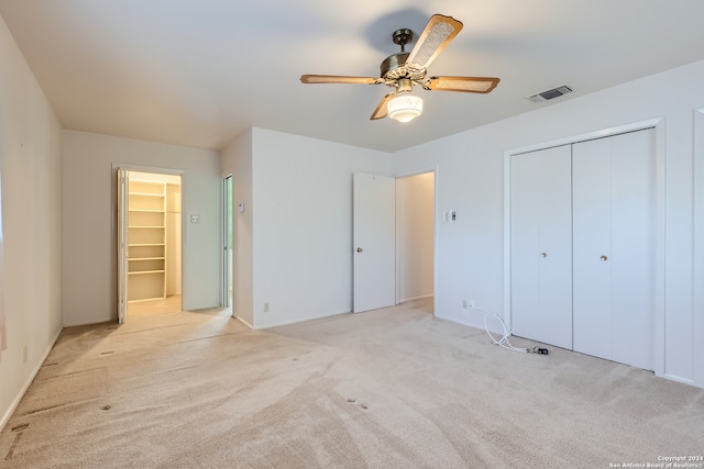 unfurnished bedroom with light carpet, a walk in closet, and ceiling fan