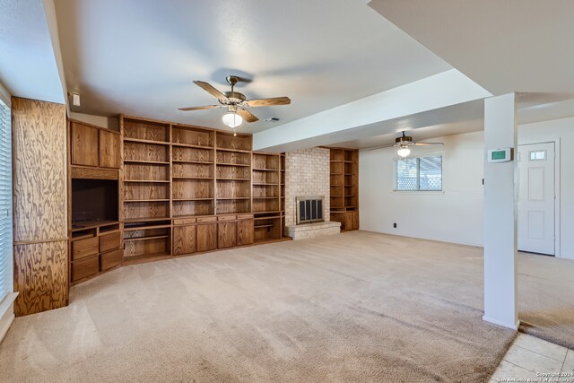 unfurnished living room featuring a brick fireplace, light colored carpet, built in shelves, and ceiling fan