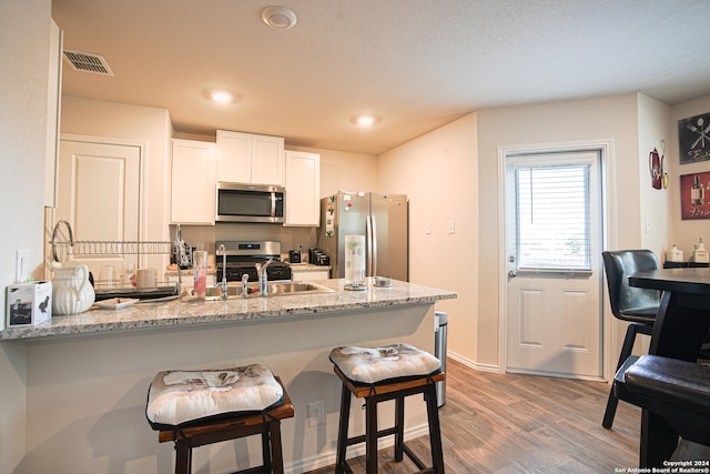 kitchen with kitchen peninsula, appliances with stainless steel finishes, light wood-type flooring, light stone counters, and white cabinets