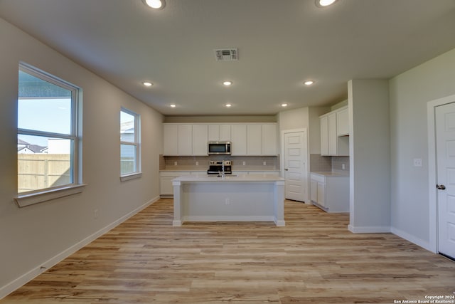 kitchen featuring a center island with sink, light wood-type flooring, tasteful backsplash, white cabinetry, and stainless steel appliances