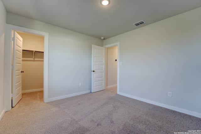 unfurnished bedroom featuring a spacious closet, a closet, and light colored carpet