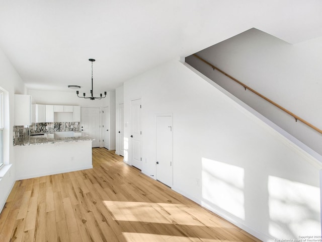 interior space featuring light stone countertops, decorative light fixtures, an inviting chandelier, light wood-type flooring, and white cabinetry