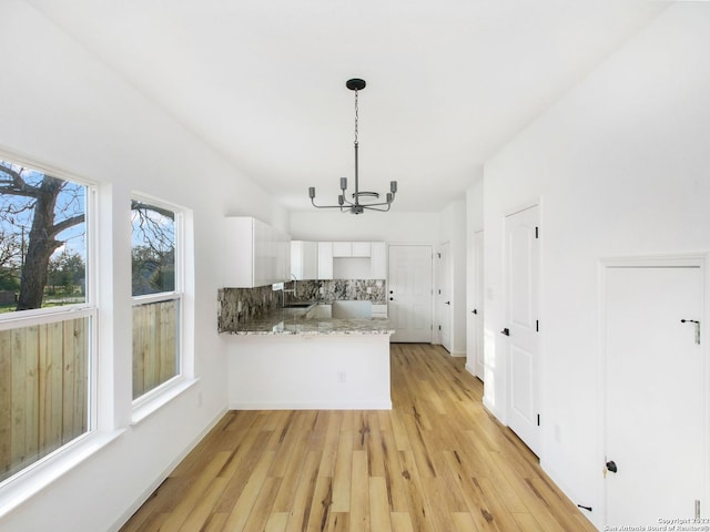 kitchen with kitchen peninsula, white cabinets, an inviting chandelier, light wood-type flooring, and decorative light fixtures