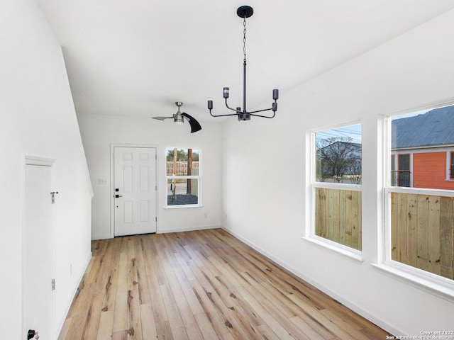 unfurnished dining area featuring a wealth of natural light, light wood-type flooring, and ceiling fan with notable chandelier