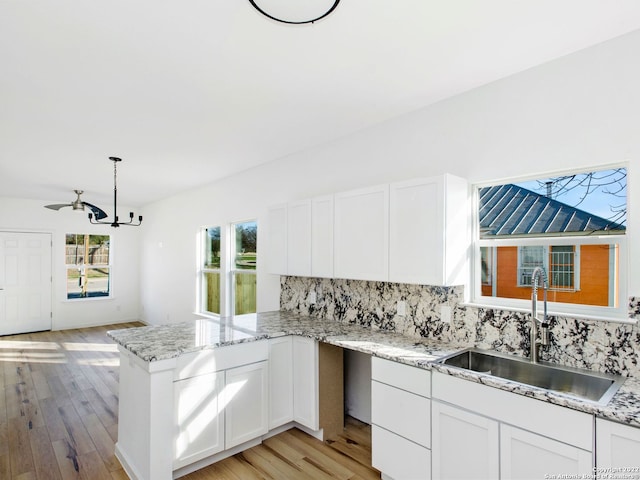 kitchen featuring kitchen peninsula, white cabinetry, light hardwood / wood-style flooring, sink, and decorative light fixtures