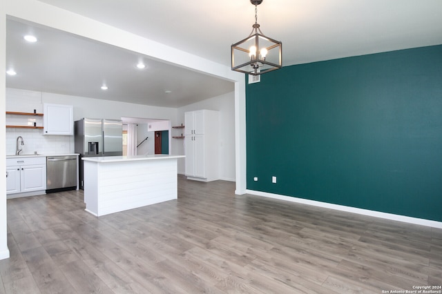 kitchen with appliances with stainless steel finishes, a kitchen island, hanging light fixtures, light hardwood / wood-style floors, and white cabinets