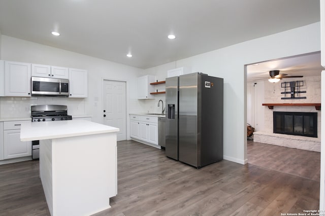 kitchen featuring a kitchen island, a stone fireplace, dark hardwood / wood-style flooring, stainless steel appliances, and white cabinets