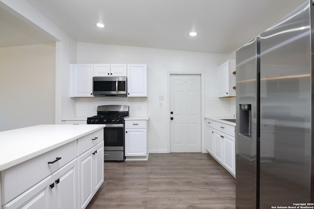 kitchen with white cabinets, tasteful backsplash, hardwood / wood-style floors, appliances with stainless steel finishes, and vaulted ceiling