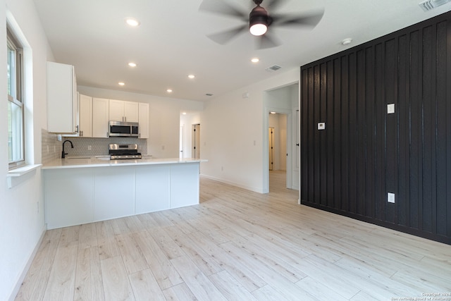 kitchen featuring appliances with stainless steel finishes, kitchen peninsula, white cabinets, and light hardwood / wood-style floors