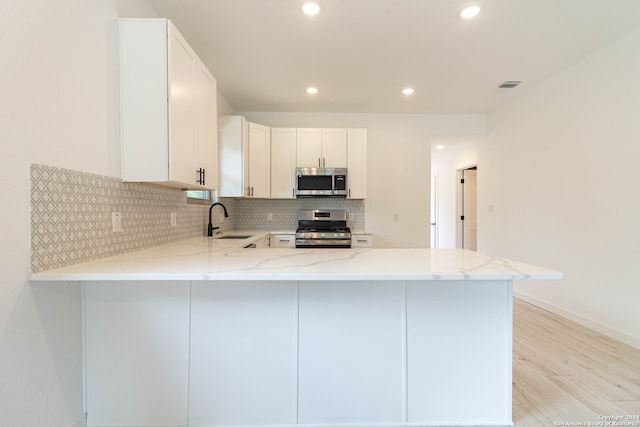 kitchen with kitchen peninsula, white cabinets, stainless steel appliances, and sink