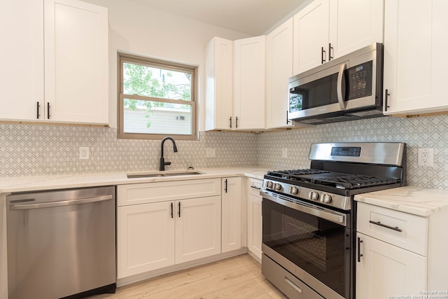 kitchen with tasteful backsplash, light wood-type flooring, stainless steel appliances, white cabinets, and light stone counters