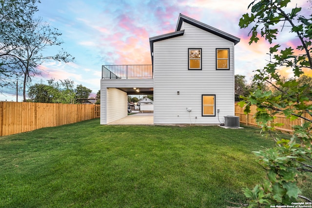 back house at dusk with central air condition unit, a patio area, and a lawn