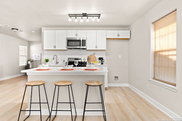 kitchen with stainless steel appliances, an island with sink, light hardwood / wood-style floors, a kitchen bar, and white cabinets