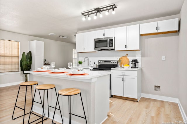 kitchen with a kitchen breakfast bar, white cabinetry, a kitchen island with sink, and appliances with stainless steel finishes