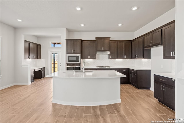 kitchen with a kitchen island with sink, stainless steel appliances, sink, dark brown cabinetry, and light hardwood / wood-style floors