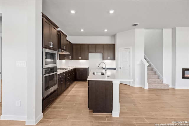 kitchen with dark brown cabinets, a center island with sink, light wood-type flooring, sink, and stainless steel appliances