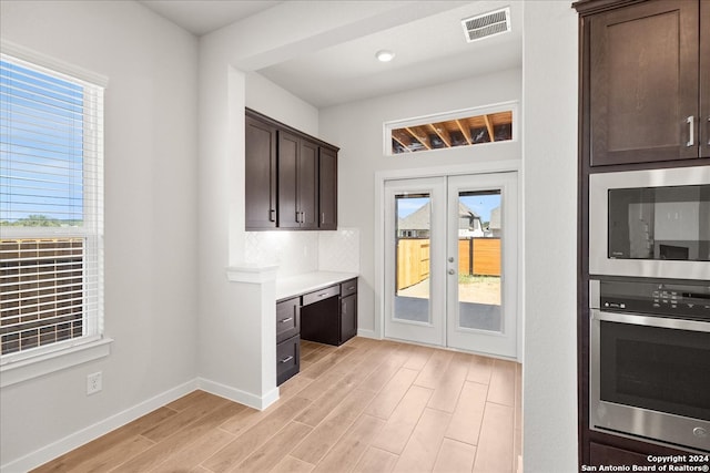 kitchen with tasteful backsplash, light wood-type flooring, built in desk, stainless steel appliances, and dark brown cabinetry