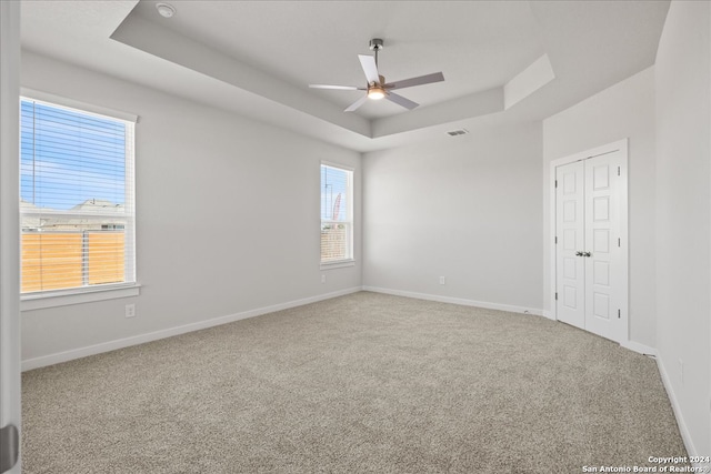 empty room with carpet floors, a tray ceiling, and ceiling fan