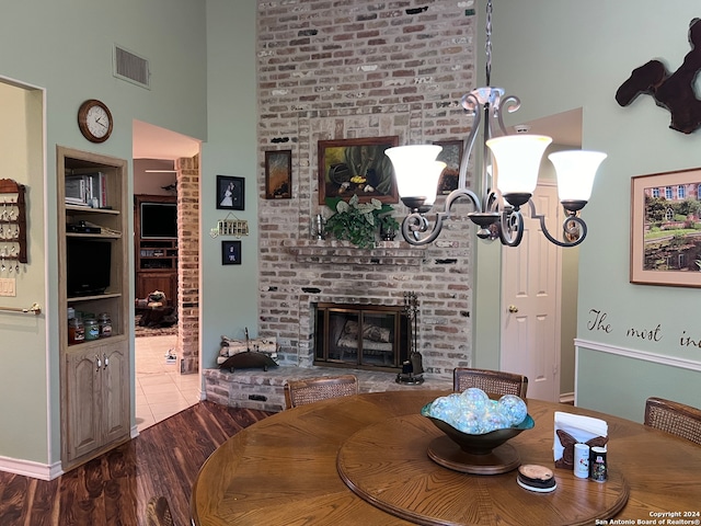 dining space featuring a high ceiling, an inviting chandelier, a fireplace, and hardwood / wood-style floors