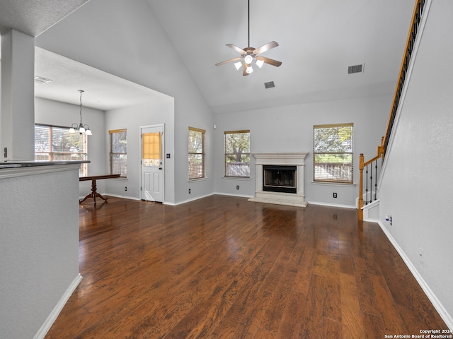 unfurnished living room with ceiling fan with notable chandelier, high vaulted ceiling, and dark hardwood / wood-style flooring