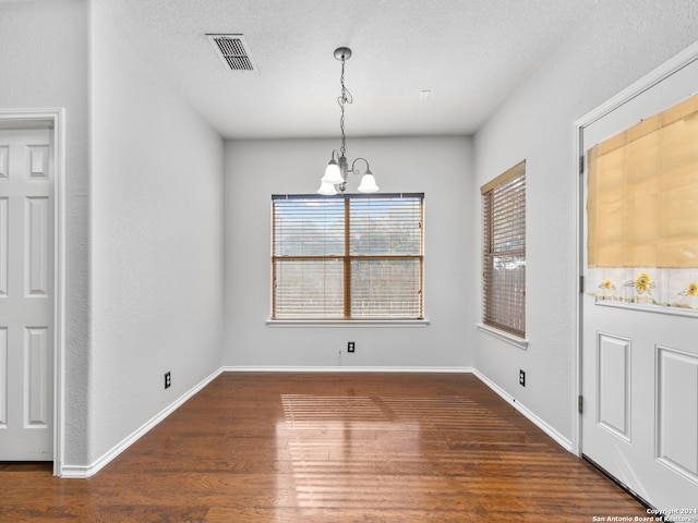 unfurnished dining area with a notable chandelier, a textured ceiling, and dark hardwood / wood-style flooring