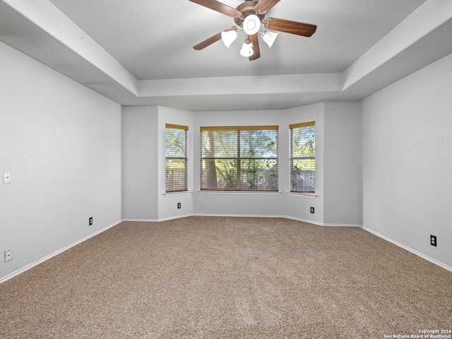 carpeted empty room featuring ceiling fan and a raised ceiling