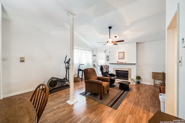 living room with wood-type flooring, a textured ceiling, a tile fireplace, ceiling fan, and lofted ceiling